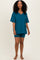 woman wearing a teal v-neck oversized t-shirt and matching fitted shorts, standing barefoot
