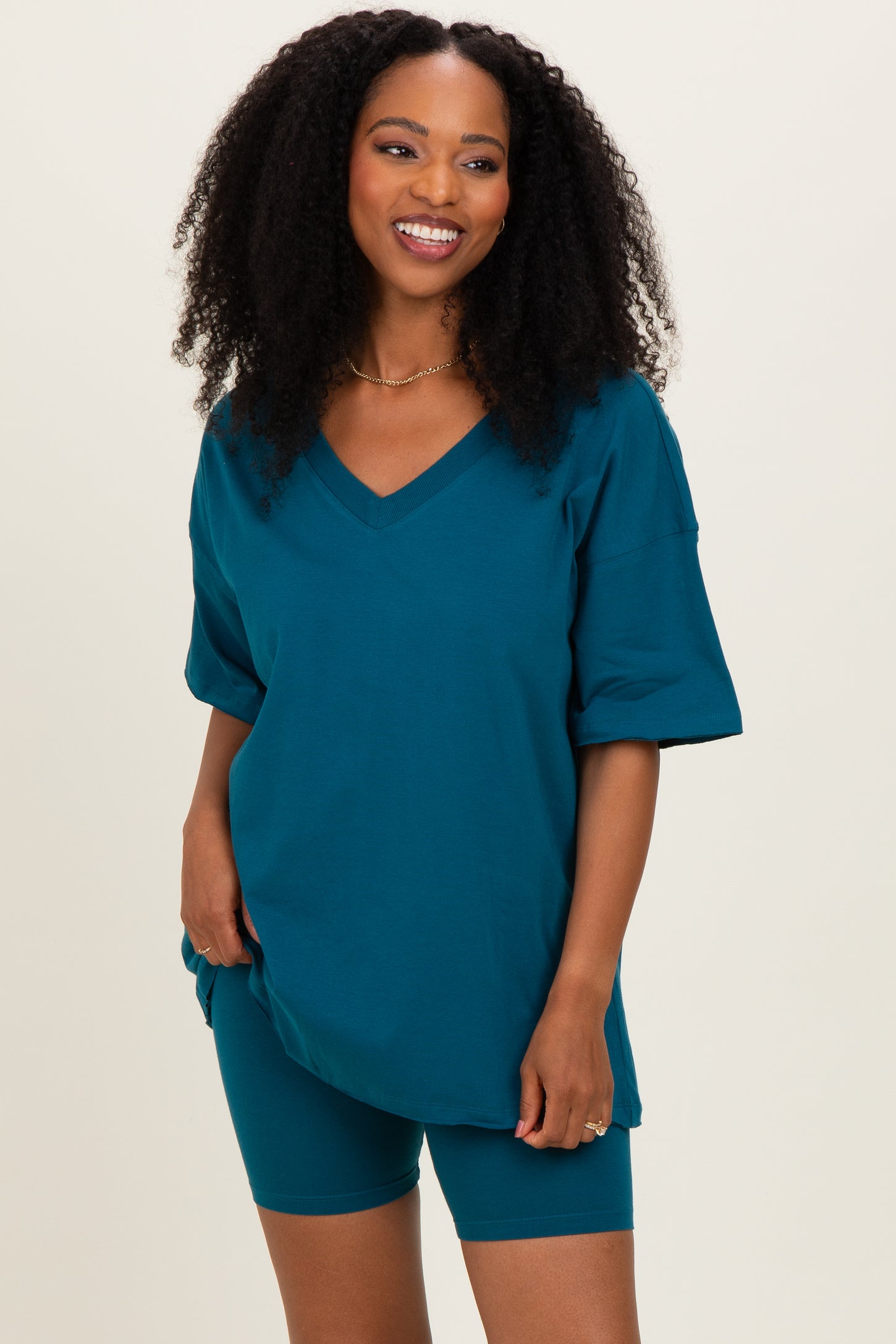 woman wearing a teal oversized v-neck t-shirt and matching bike shorts, smiling at the camera