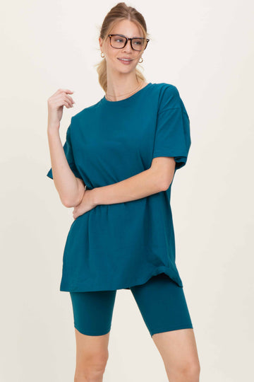 woman wearing a teal oversized t-shirt and matching biker shorts, styled with glasses and a casual pose
