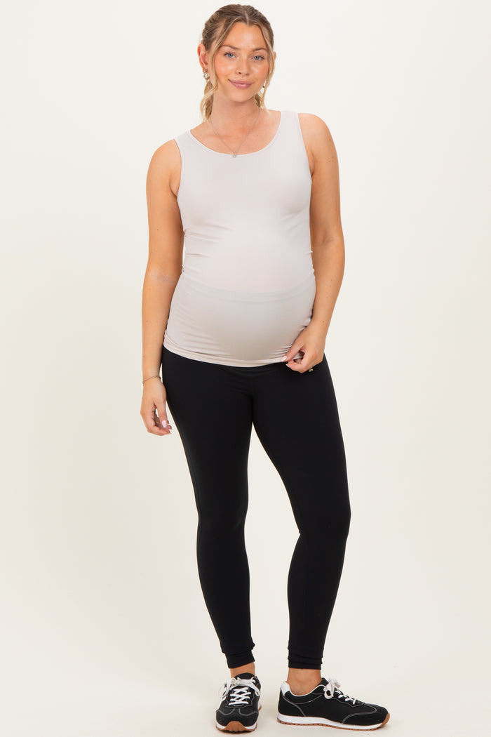 woman wearing a light gray maternity tank top and black maternity leggings, showing her baby bump