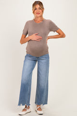 woman wearing a gray short sleeve maternity top and light blue wide-leg jeans, holding her baby bump