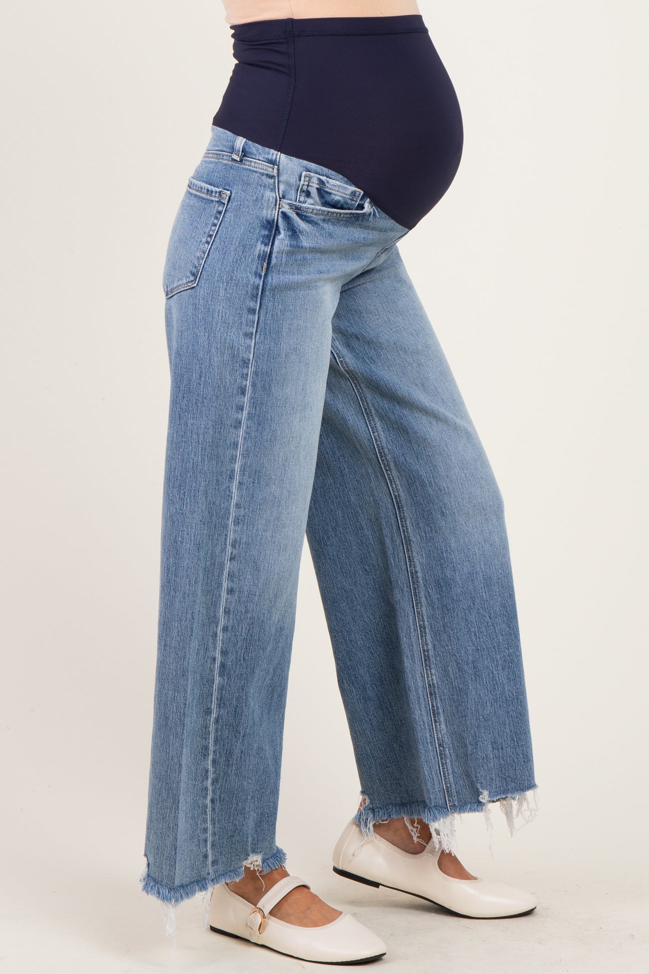 woman wearing light blue wide-leg maternity jeans with a frayed hem and a navy blue over-the-bump waistband, showing baby bump