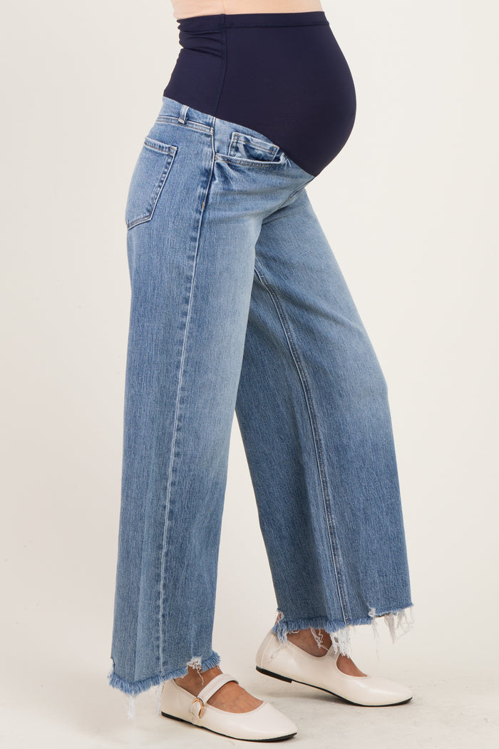 woman wearing light blue wide-leg maternity jeans with a frayed hem and a navy blue over-the-bump waistband, showing baby bump
