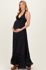 woman wearing a black maternity maxi dress with a halter neckline and tiered skirt, gently holding her baby bump