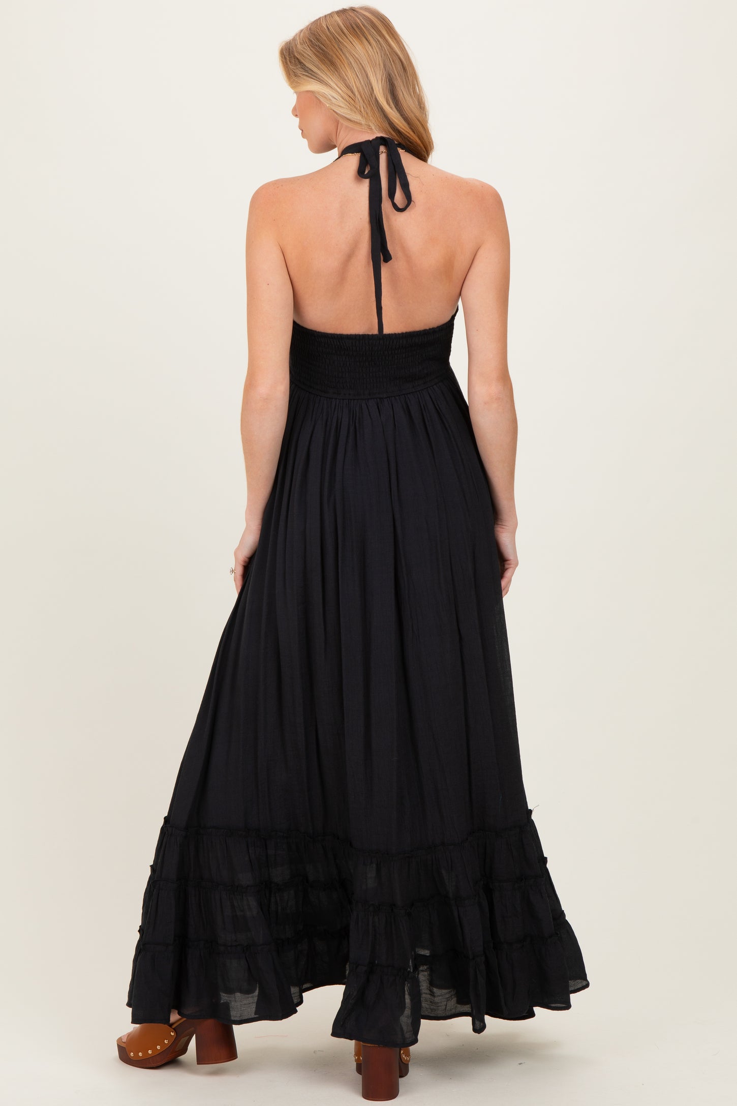 woman wearing a black halter neck maternity maxi dress with a smocked bodice and tiered ruffle hem