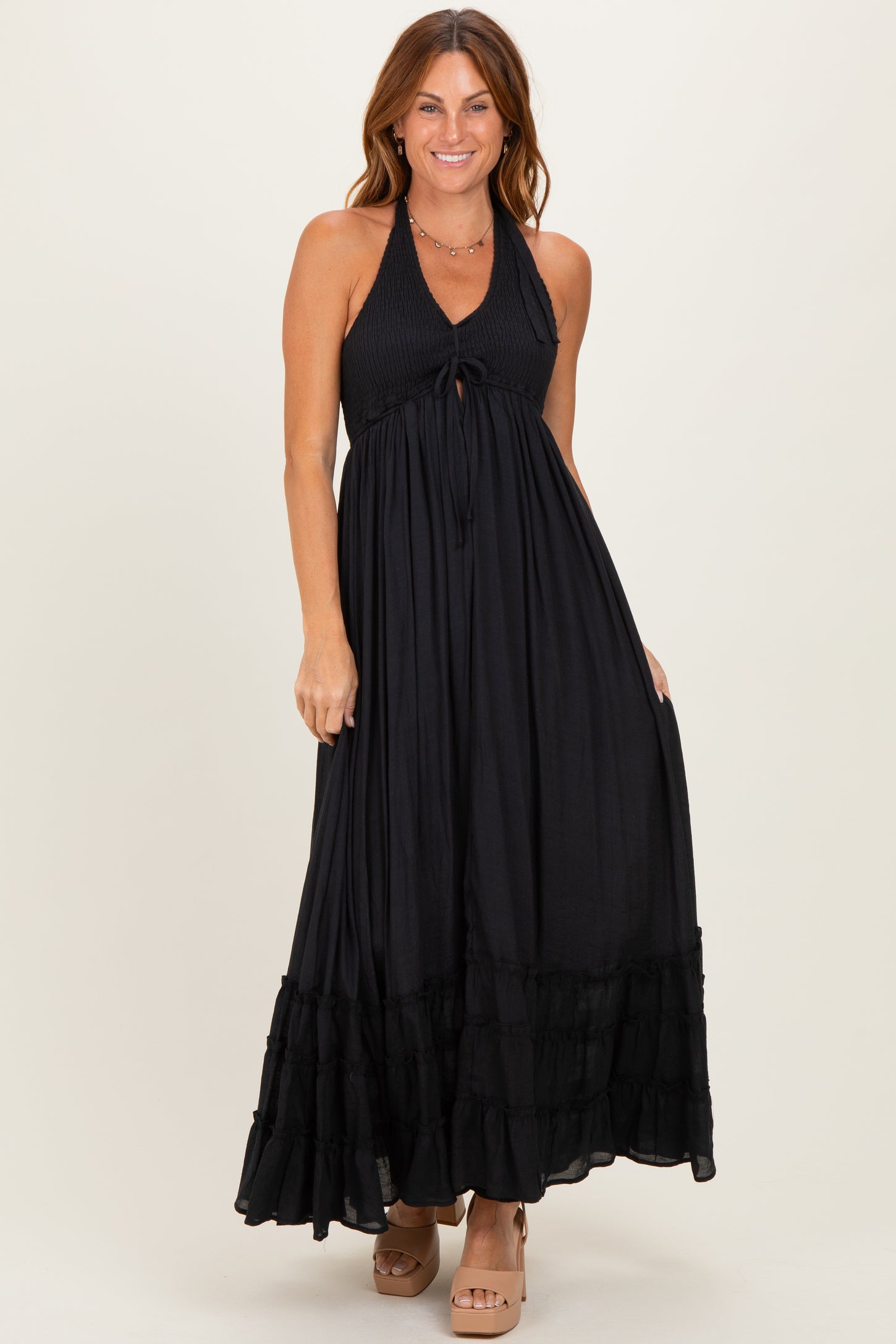 woman wearing a black halter neck maxi dress with a tie front and ruffled hem, standing and smiling