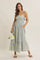 woman wearing a light blue floral maxi dress with tie straps and pockets, holding a bouquet of flowers