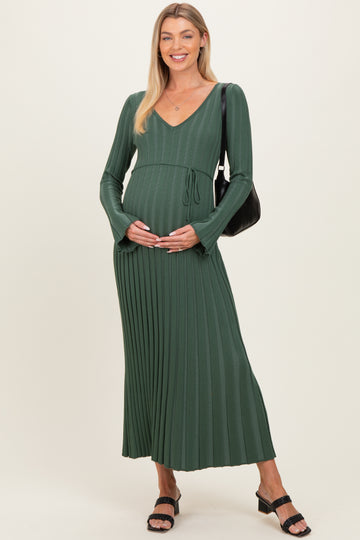 woman wearing a green long sleeve maternity dress with pleats, holding her baby bump