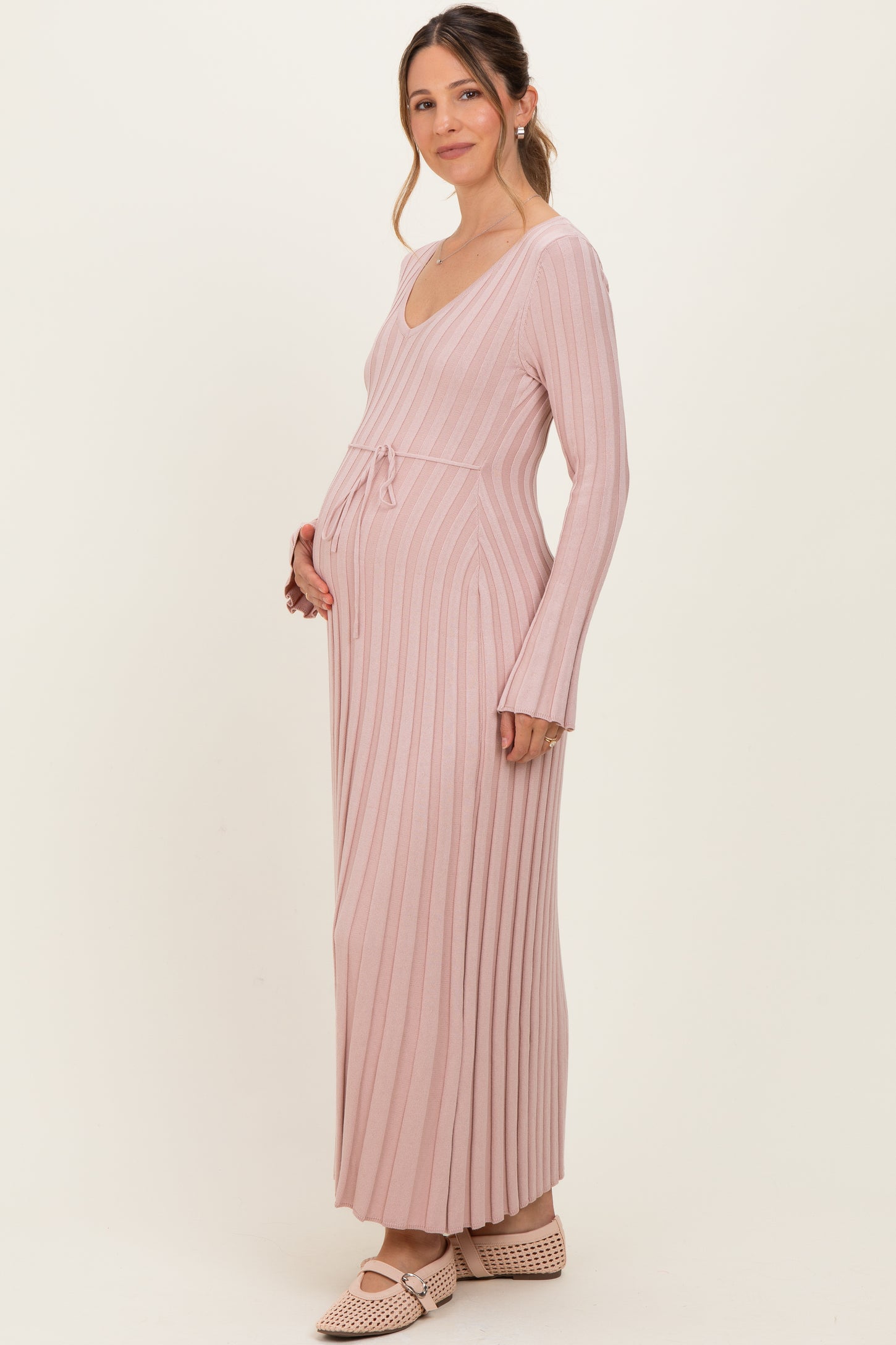 woman wearing a blush pink long sleeve ribbed maternity dress with a tie waist and visible baby bump
