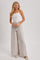 woman wearing a white smocked crop top and light gray wide-leg pants, standing with hands on hips