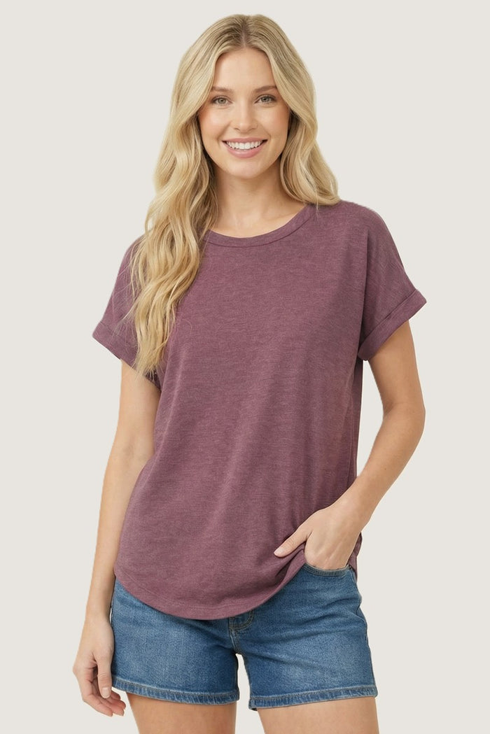 woman wearing a maroon short sleeve t-shirt with rolled cuffs and blue denim shorts, smiling at the camera