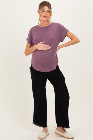 woman wearing a mauve short sleeve maternity top and black wide-leg maternity pants, holding her baby bump