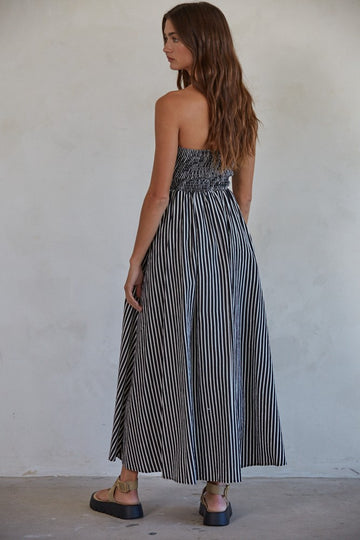woman wearing a strapless black and white striped maxi dress, showing a smocked bodice and flowy skirt from the back
