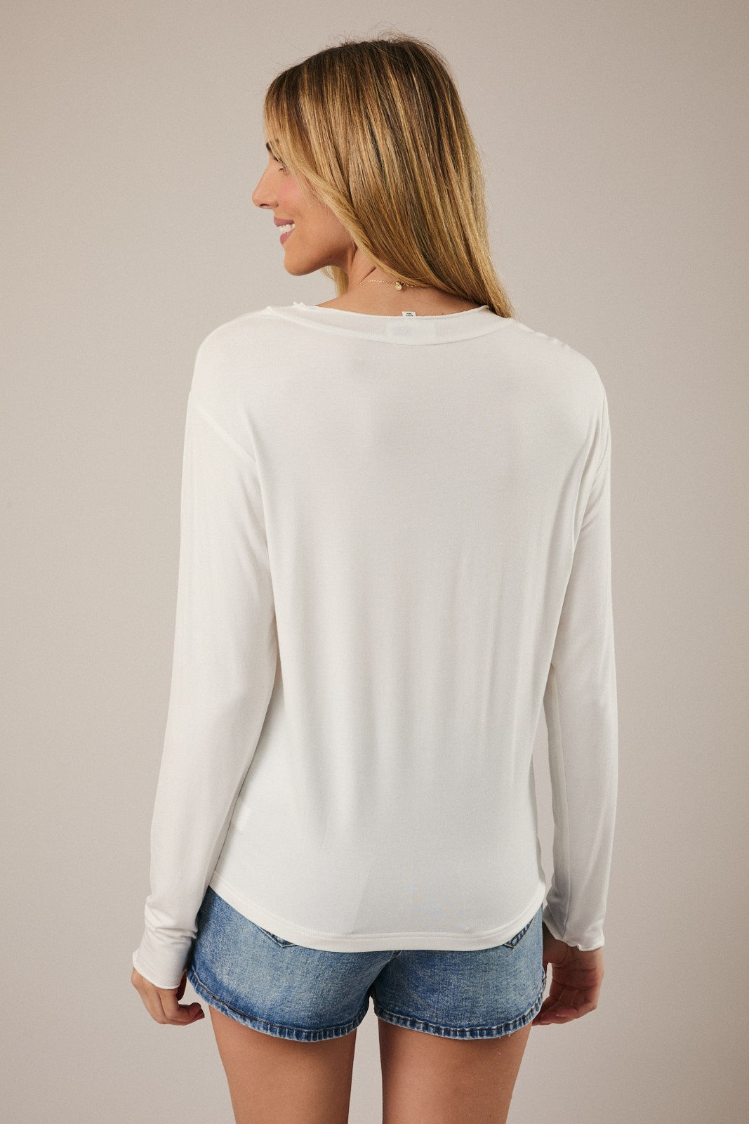 woman wearing a white long sleeve top with a relaxed fit, showing the back view, paired with denim shorts