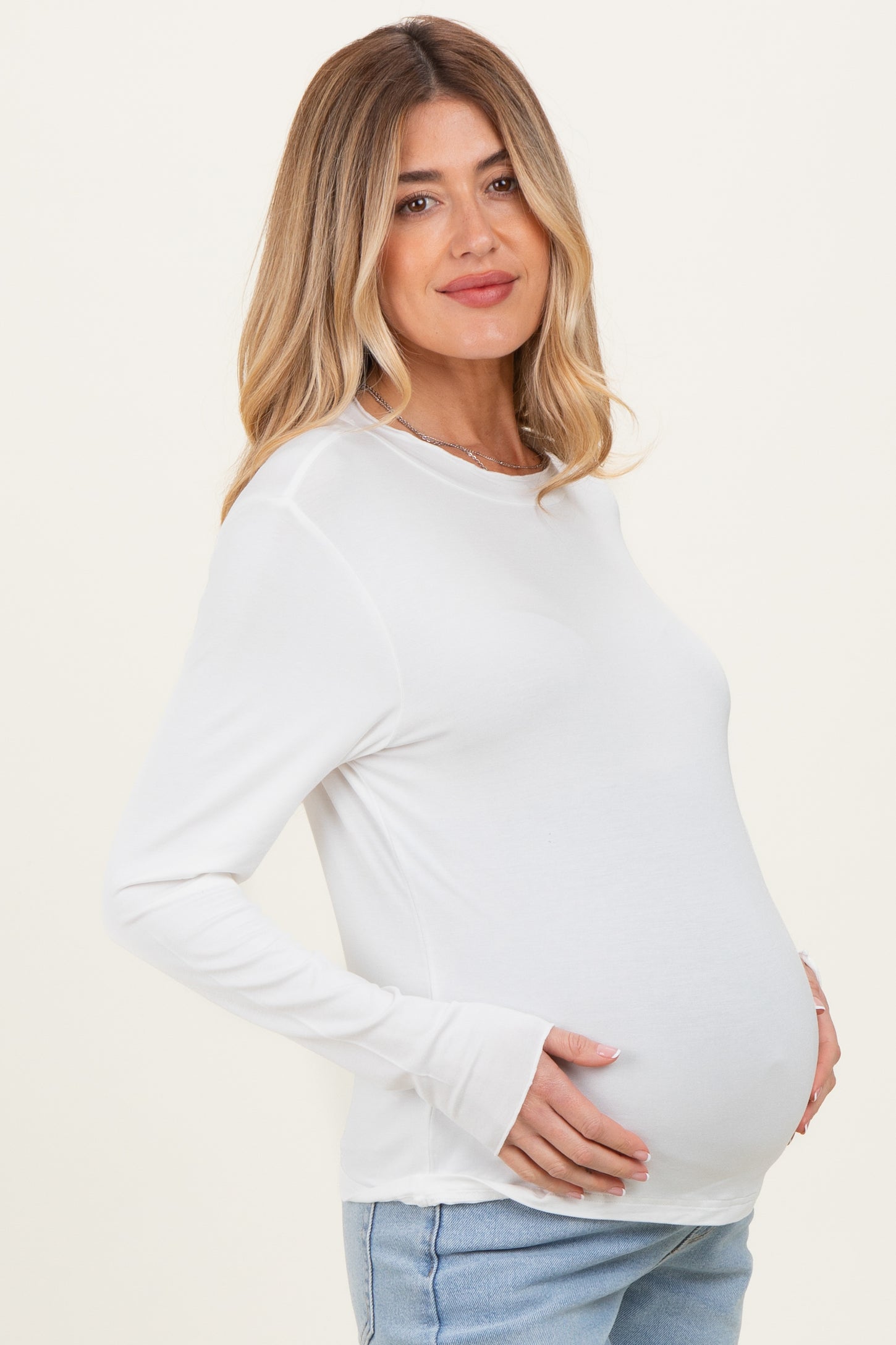 woman wearing a white long sleeve maternity top and holding her baby bump