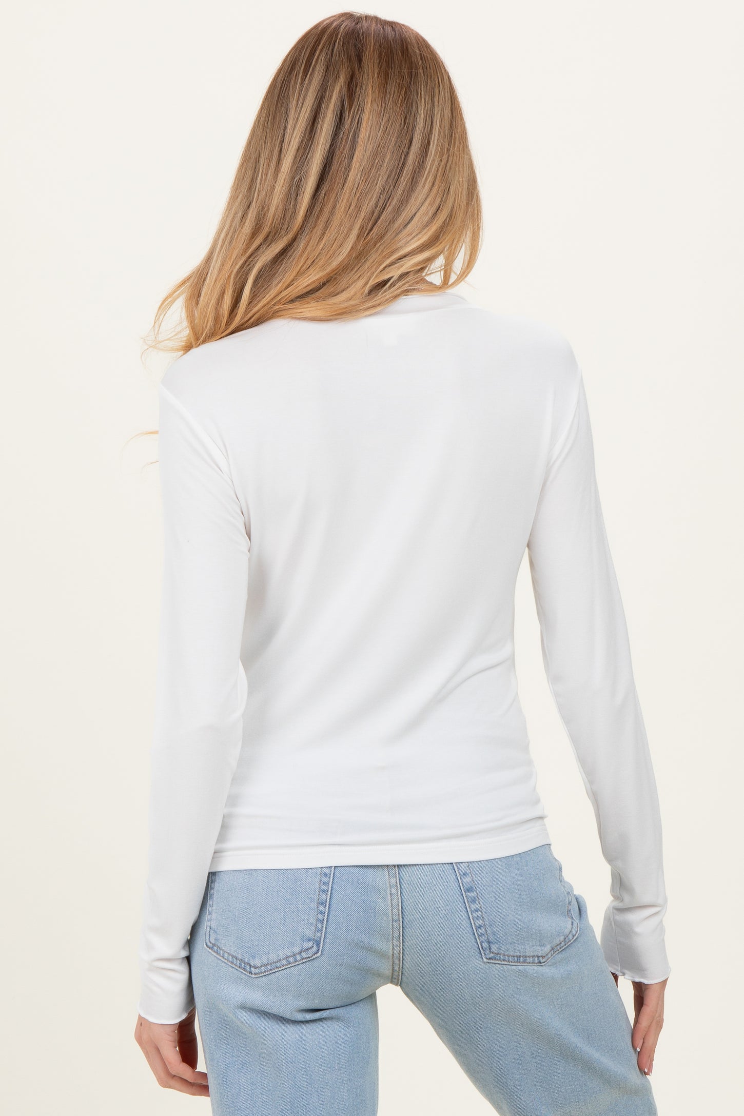woman wearing a white long sleeve maternity top and blue jeans, showing the back view of the top