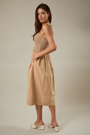 woman wearing a beige sleeveless dress with a smocked bodice and pockets, styled with open-toe heels