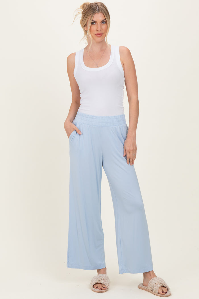 woman wearing a white ribbed tank top and light blue wide-leg pants, standing with hands in pockets