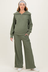 woman wearing a green ribbed maternity tracksuit with a zip-up hoodie and wide-leg pants, showing a baby bump