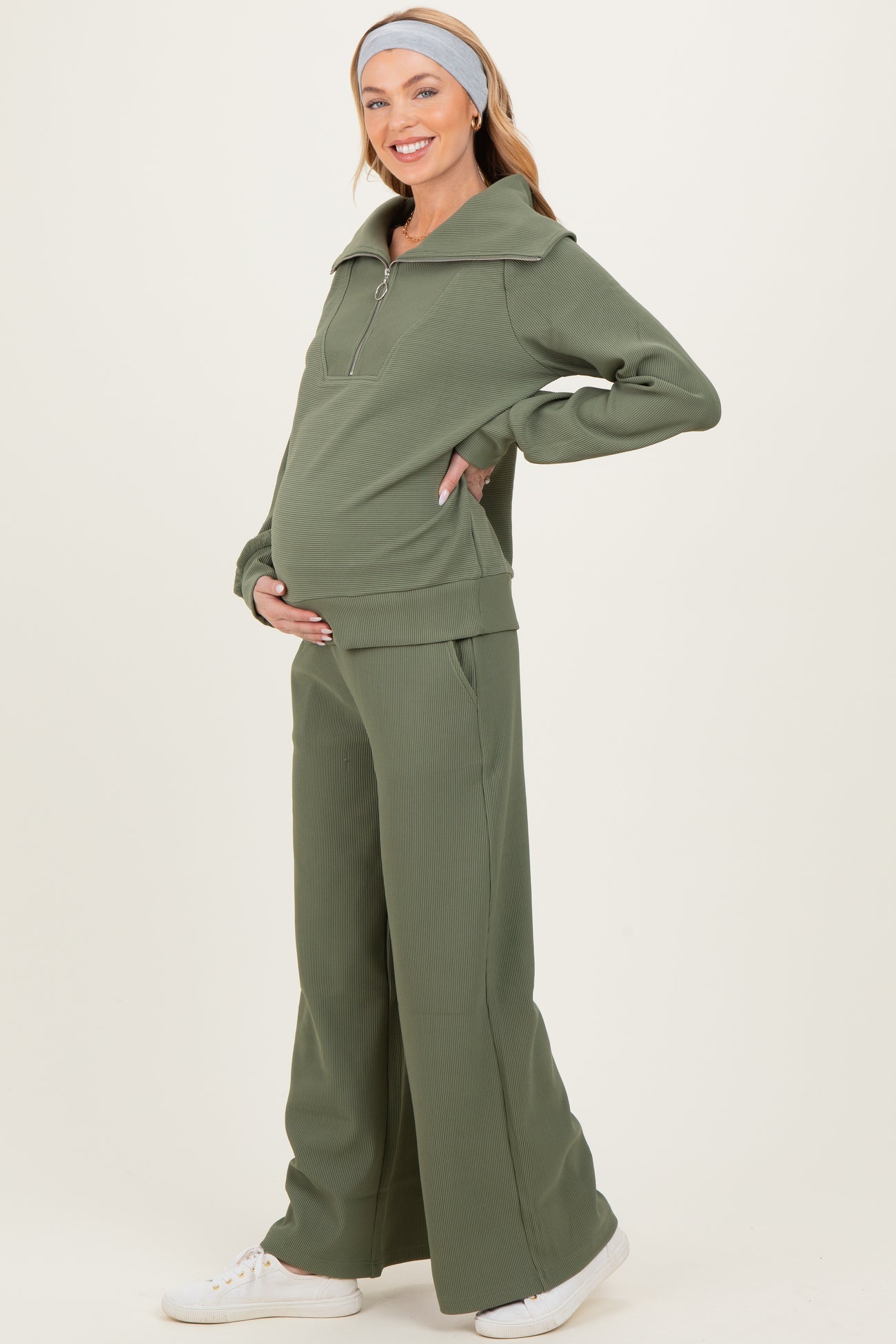 woman wearing a green ribbed maternity loungewear set with a zip-up hoodie and wide-leg pants, showing her baby bump