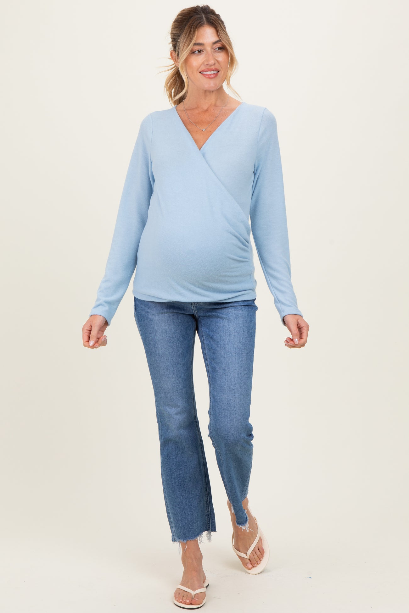 woman wearing a light blue long sleeve maternity top and jeans, showing her baby bump while walking