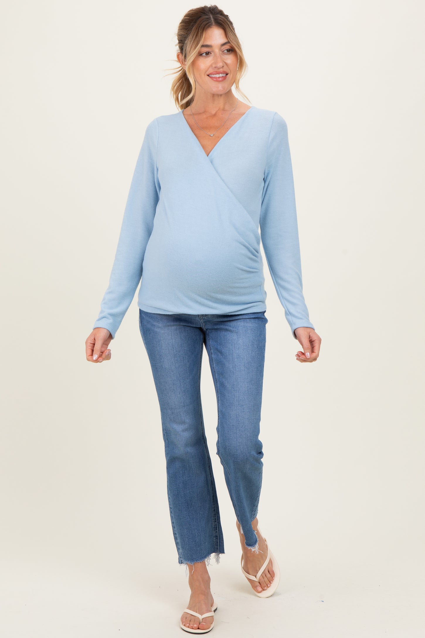 woman wearing a light blue long sleeve maternity top and jeans, showing her baby bump while walking
