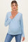 woman wearing a light blue long sleeve maternity wrap top and showcasing her baby bump
