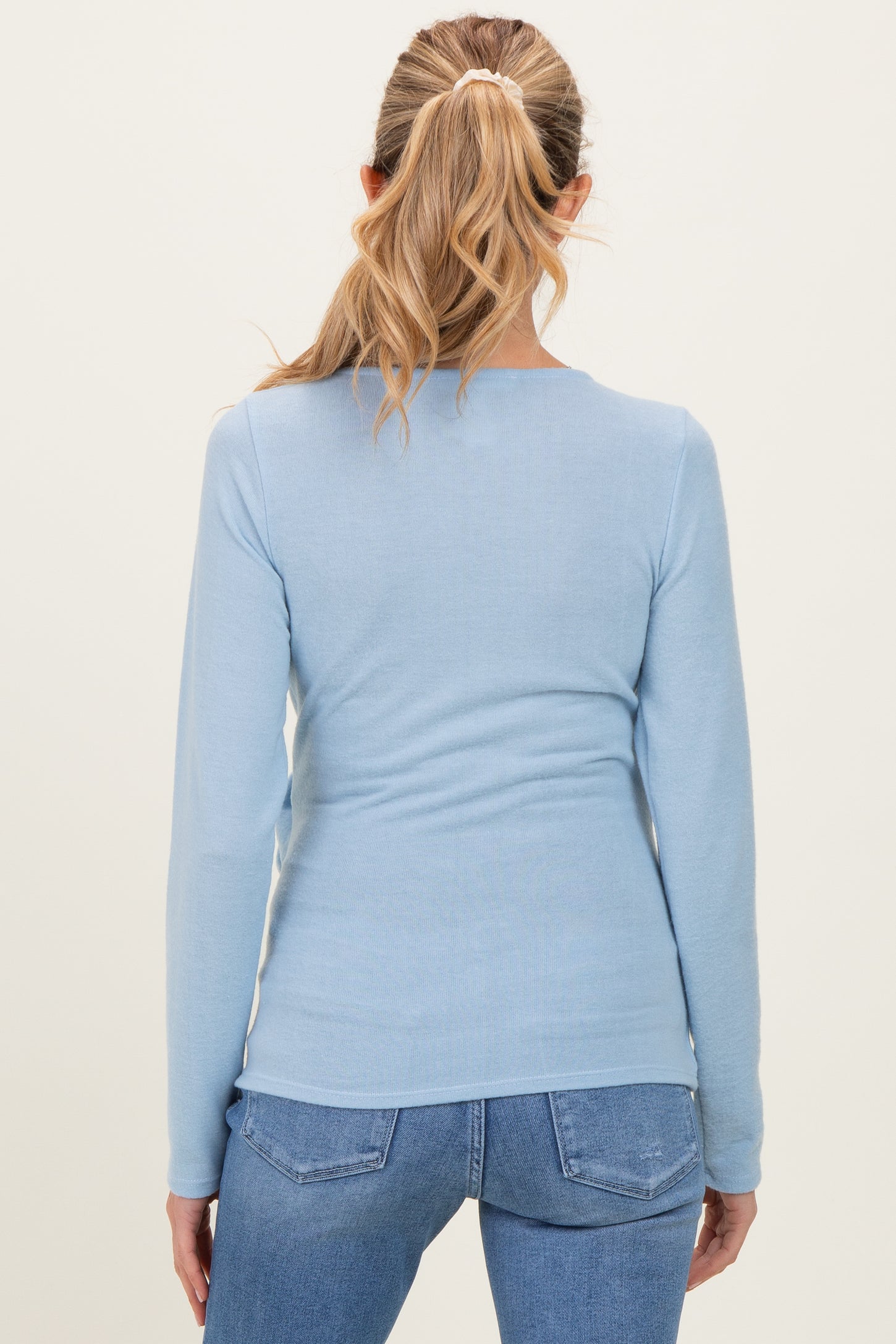 woman wearing a light blue long sleeve maternity top, viewed from the back with a fitted silhouette