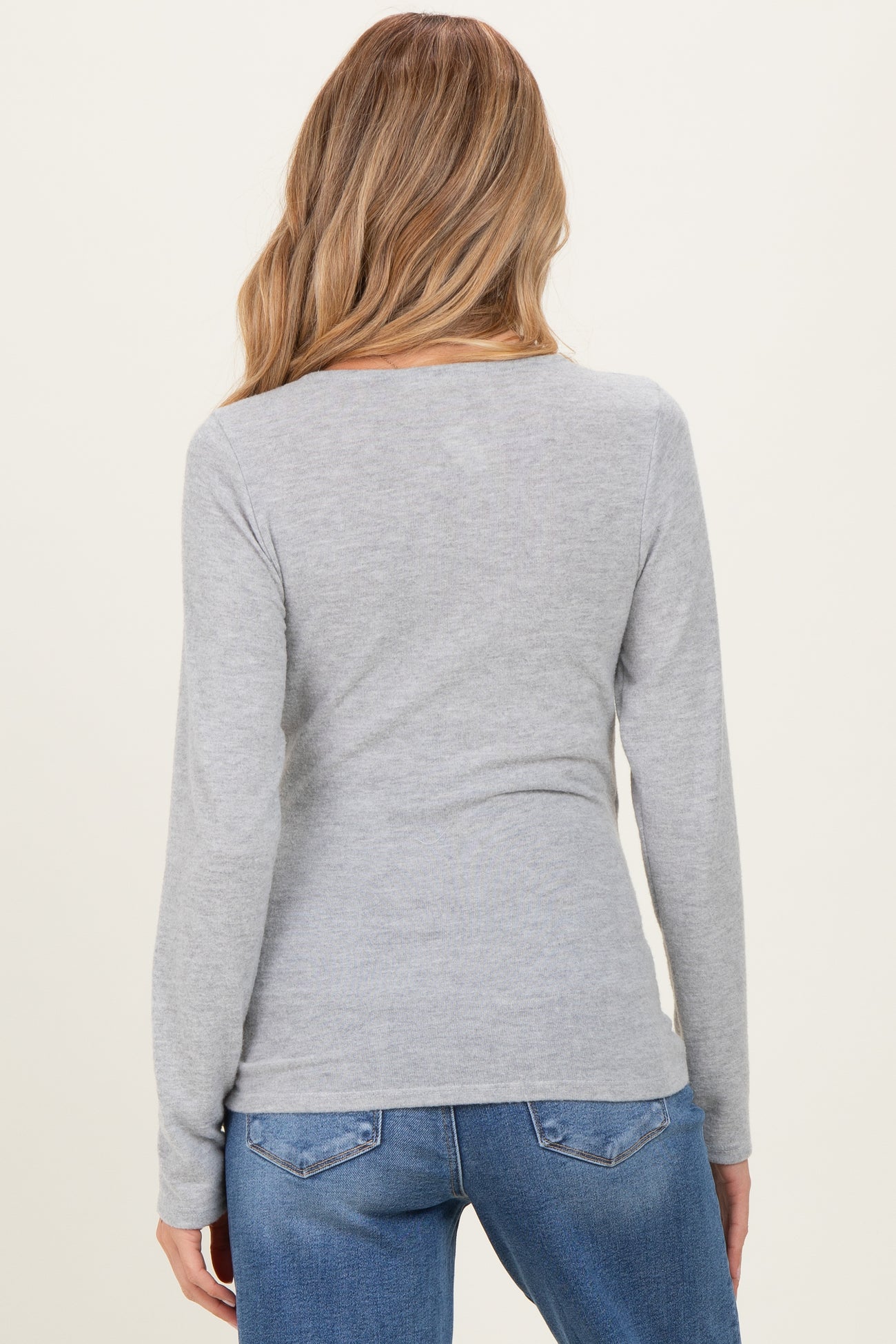 woman wearing a grey long sleeve maternity top from the back with blue jeans