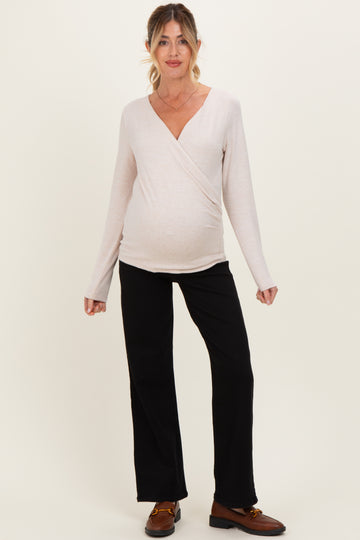 woman wearing a light pink long sleeve wrap maternity top and black flared pants with a visible baby bump