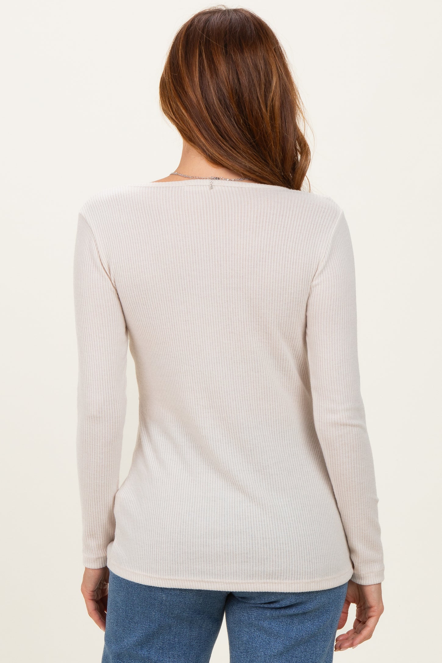 woman wearing a soft beige ribbed long sleeve top seen from the back, paired with blue jeans