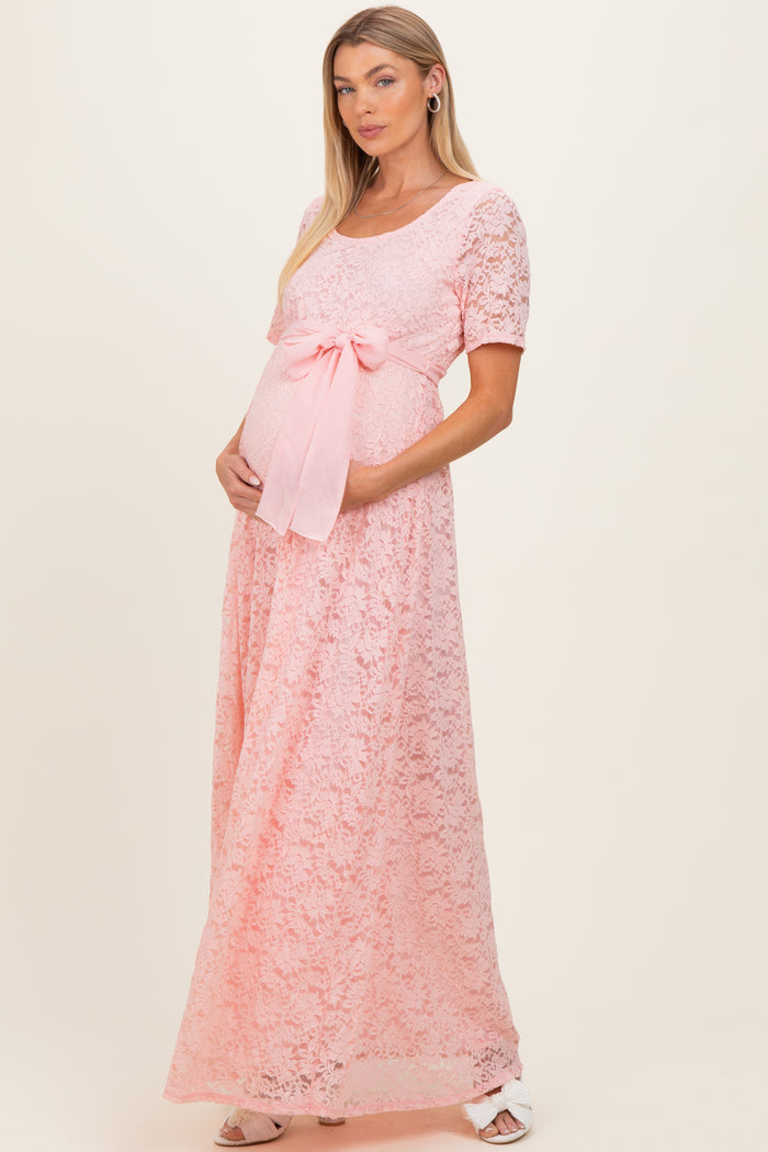 woman wearing a pink lace maternity gown with short sleeves and a bow tie at the waist, highlighting her baby bump