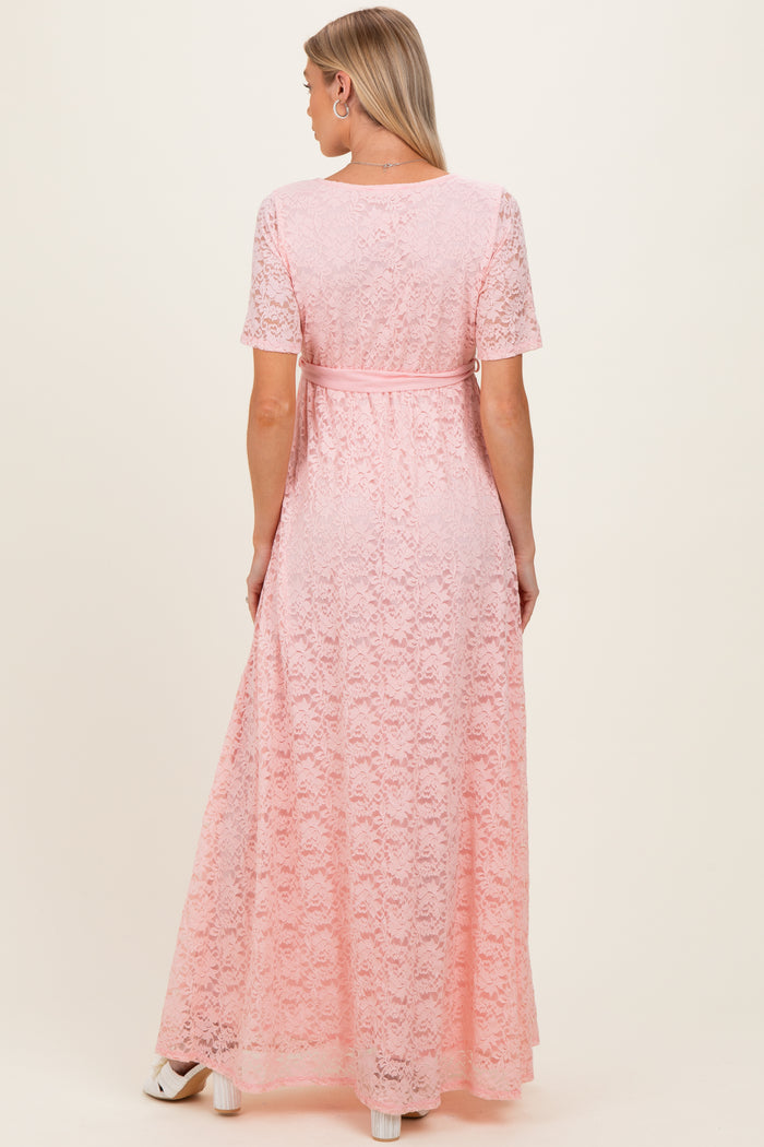 woman wearing a blush pink lace maternity maxi dress with a belted waist and short sleeves