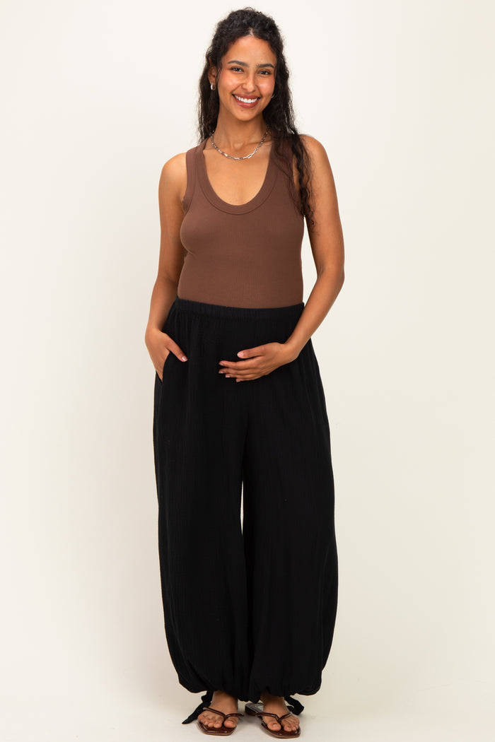woman wearing a brown ribbed maternity tank top and black maternity wide-leg pants, holding her baby bump