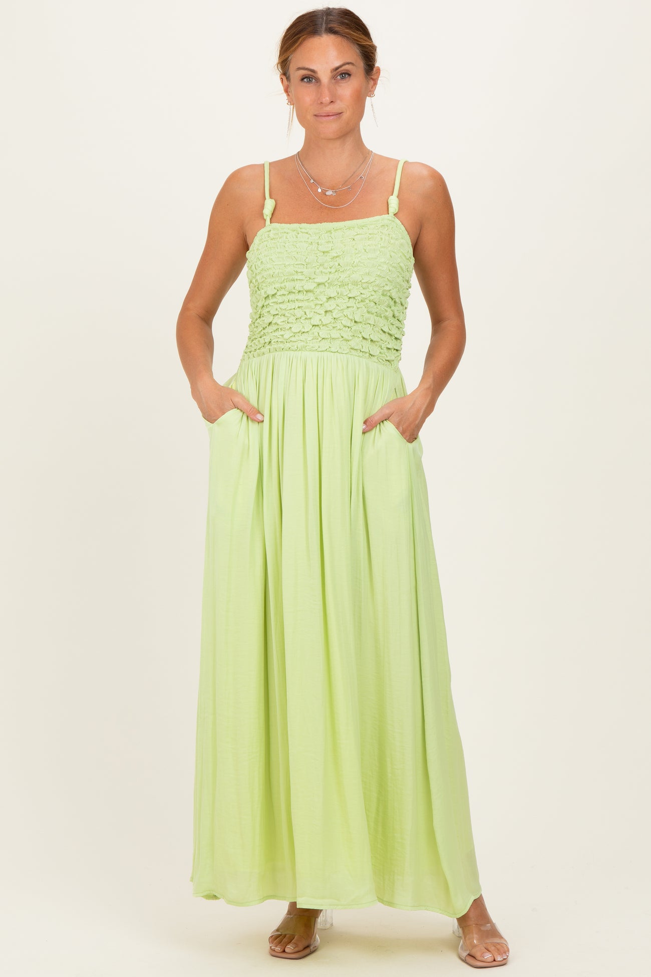 woman wearing a light green maxi dress with a smocked bodice and pockets, standing against a plain background