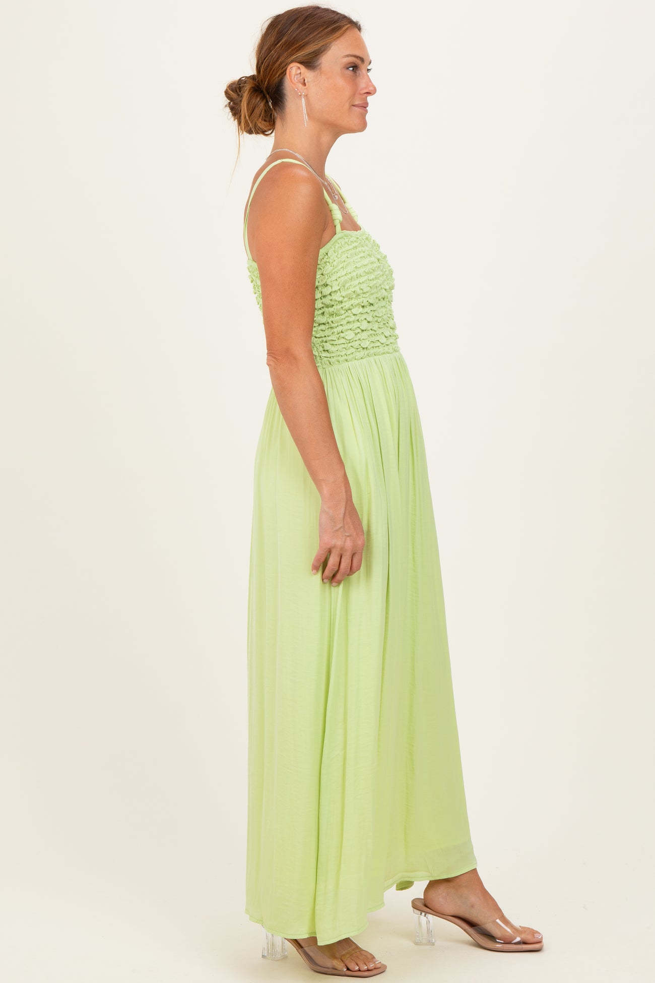 woman wearing a light green maxi dress with a smocked bodice and thin straps, standing in profile