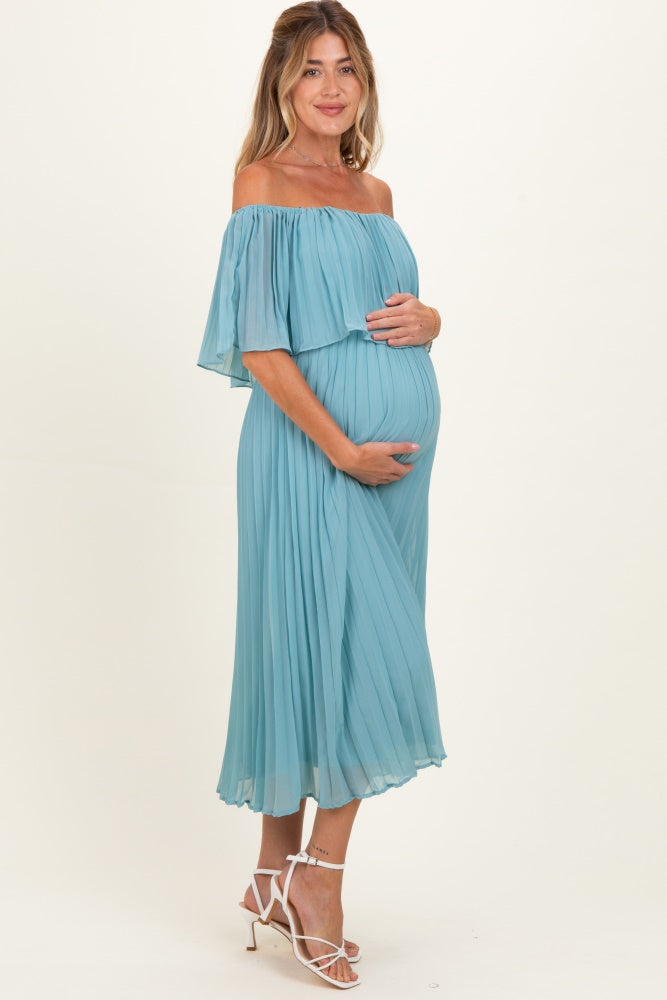 woman wearing a light blue off-the-shoulder maternity dress and holding her baby bump
