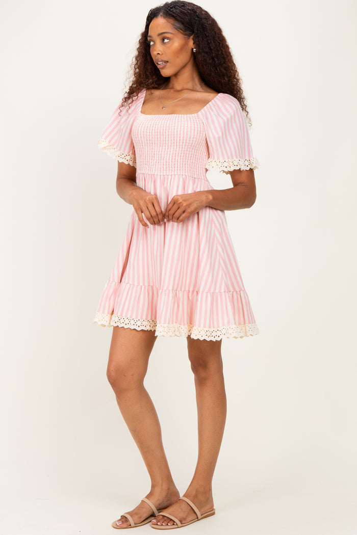 woman wearing a pink and white striped short dress with a square neckline and lace trim at the sleeves and hem