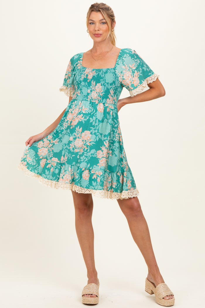 woman wearing a teal floral maternity dress with short ruffled sleeves and lace trim, showing off her baby bump
