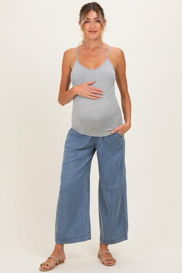 woman wearing a gray maternity tank top and blue wide-leg pants, gently holding her baby bump