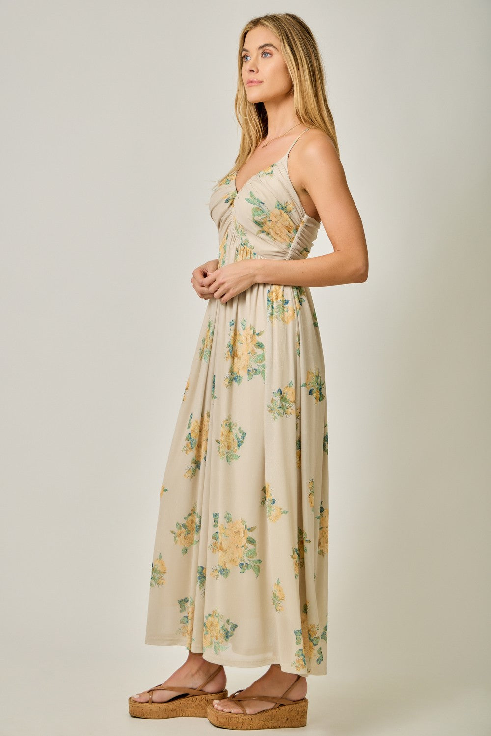 woman wearing a beige floral maxi dress with a fitted bodice and flowy skirt, standing in profile