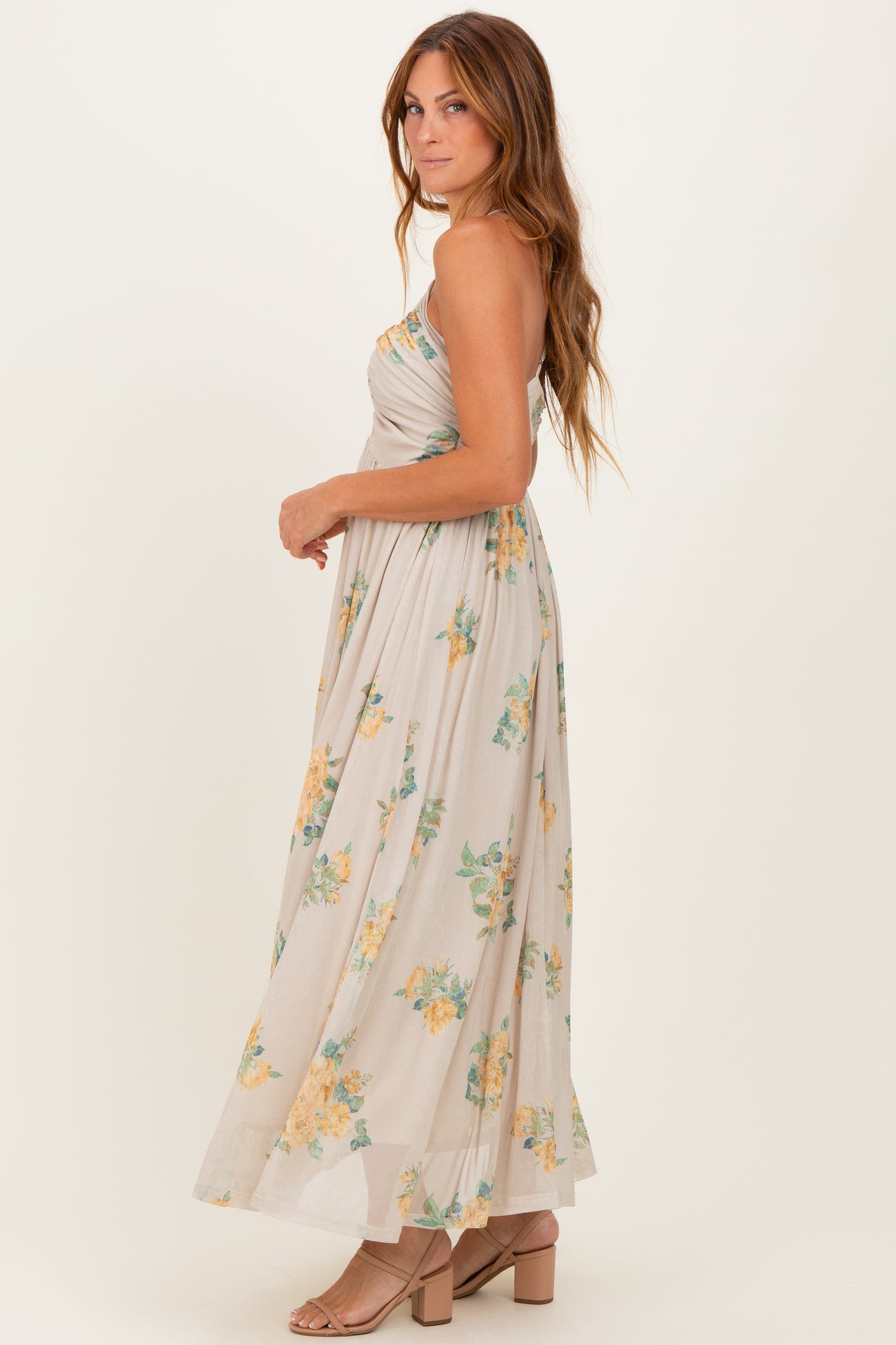 woman wearing a floral strapless maxi dress in beige with yellow and green patterns, standing sideways with a relaxed pose