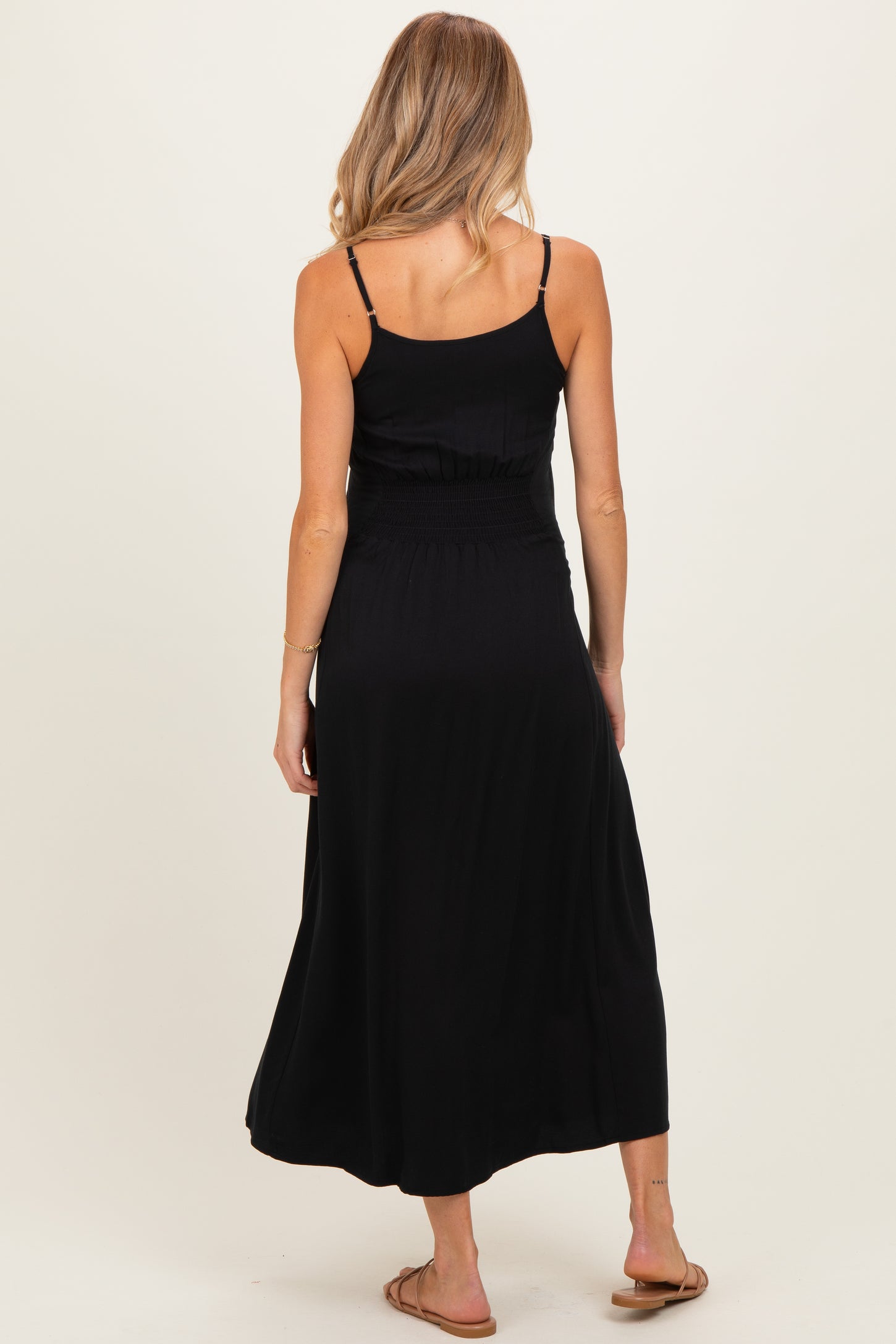 woman wearing a black maternity maxi dress with a smocked waist and adjustable spaghetti straps, showing her back