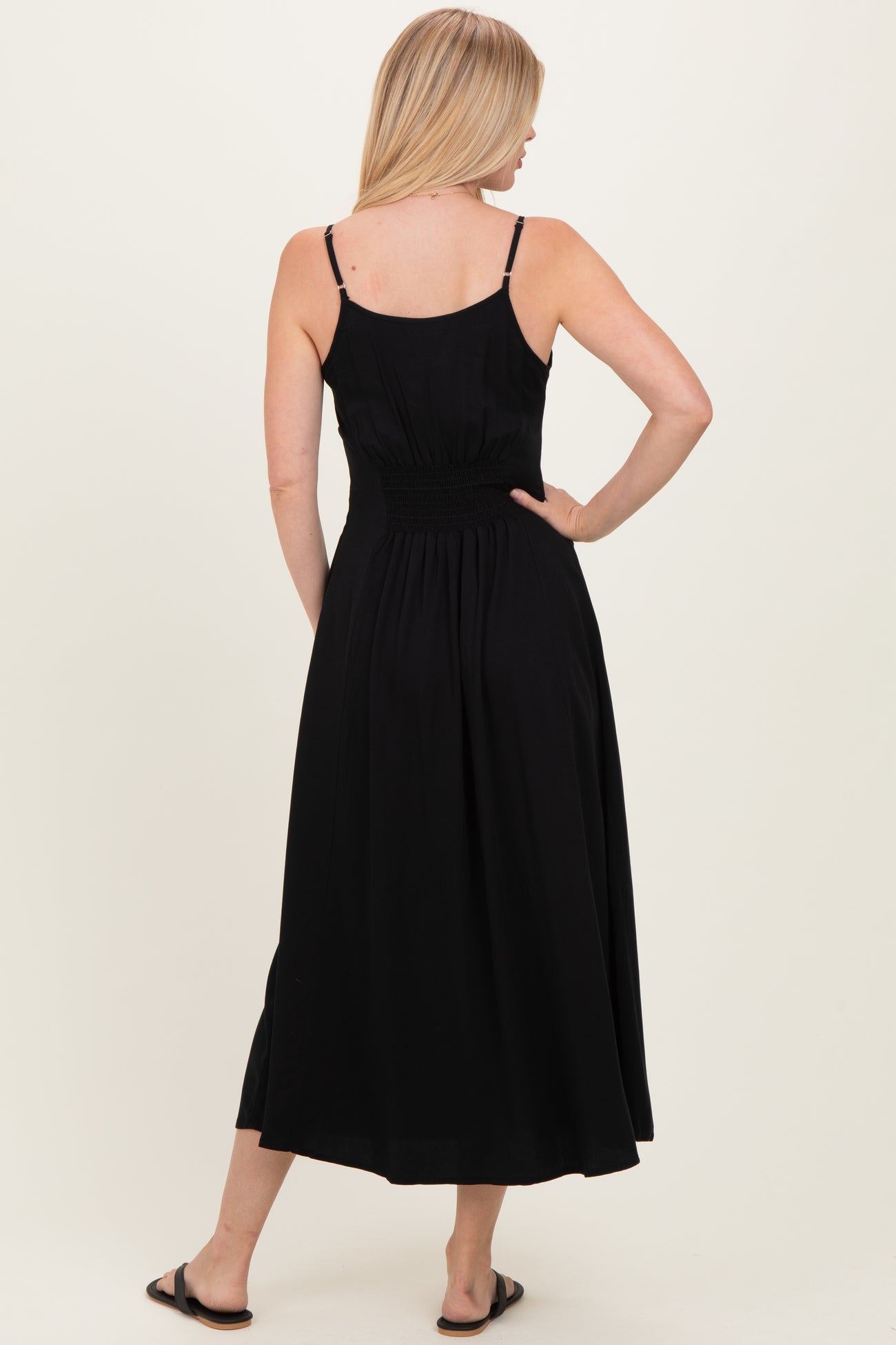 woman wearing a black sleeveless midi dress with a smocked back and flowing skirt standing sideways