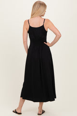 woman wearing a black sleeveless midi dress with a smocked back and flowing skirt standing sideways