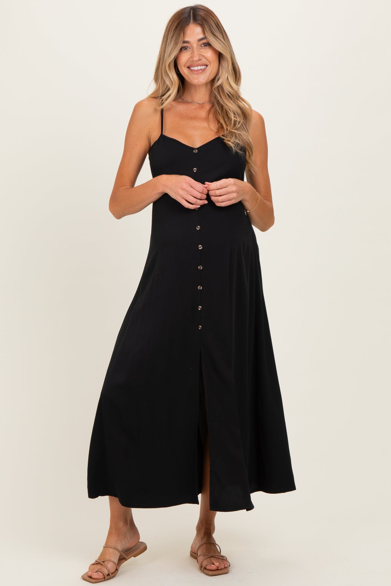 woman wearing a black maternity maxi dress with button details and adjustable straps, showing a baby bump