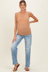 woman wearing a tan maternity tank top and light blue jeans, showing her baby bump while standing and smiling