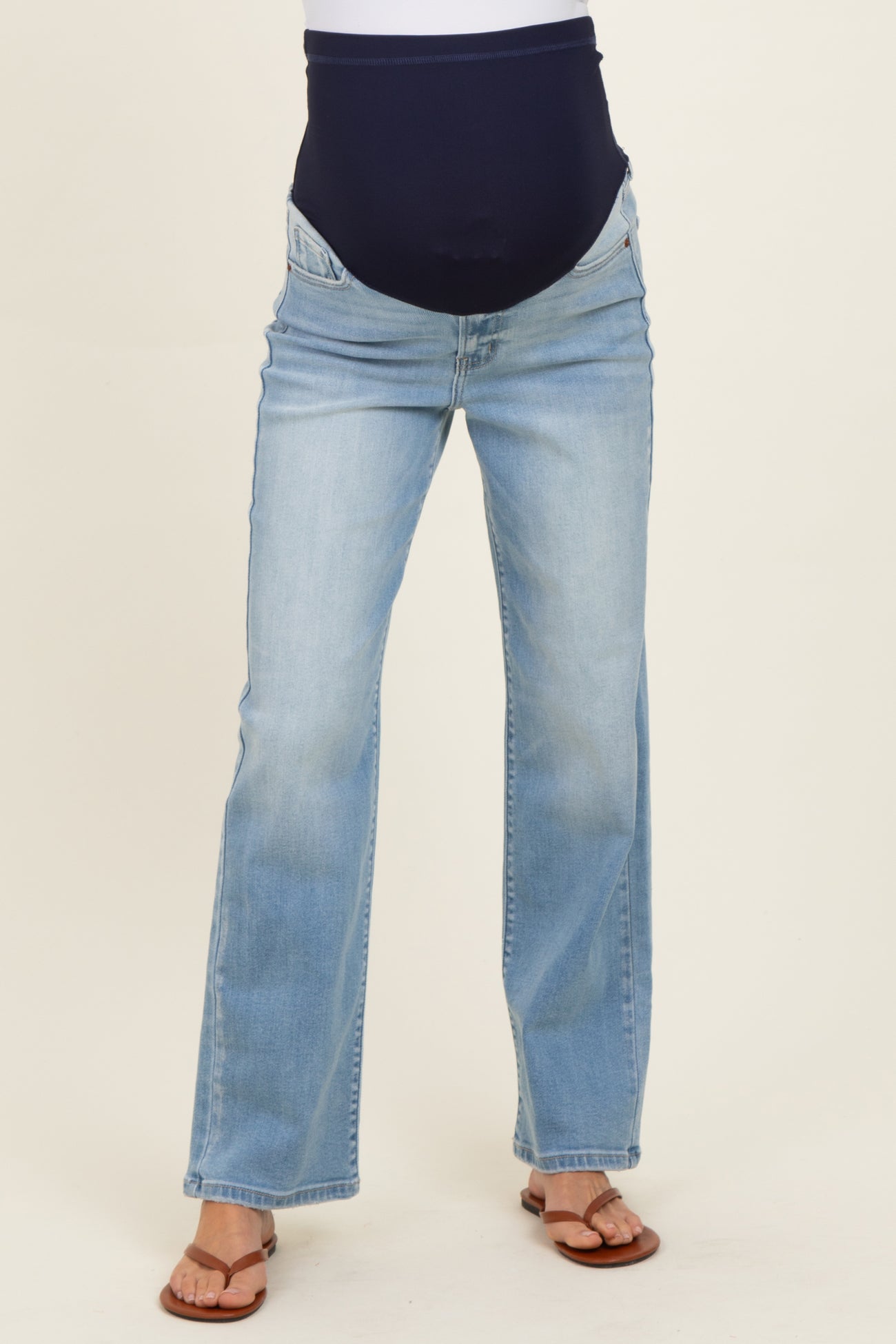 woman wearing light blue maternity jeans with a dark blue over-the-bump waistband and brown sandals