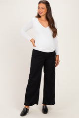 woman wearing a white long sleeve maternity top and black wide-leg maternity pants with a visible baby bump