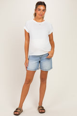 woman wearing a white short sleeve maternity top and denim shorts, with a visible baby bump